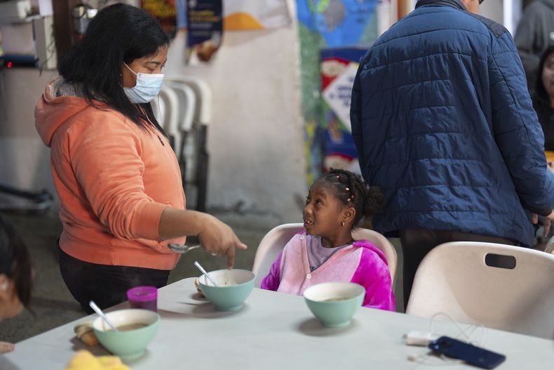 Maickeliys Rodríguez, de 6 años, de Venezuela, a la derecha, hace un gesto mientras su madre Margelis le dice que se tome el desayuno en el refugio para migrantes donde se alojan en Tijuana, México, el sábado 1 de febrero de 2025. (AP Foto/Gregory Bull)