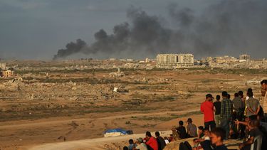 Palestinos desplazados observan cómo se eleva el humo por los ataques del ejército israelí mientras se reúnen en la carretera costera cerca de Wadi Gaza, en el centro de la Franja de Gaza, el jueves 9 de octubre de 2025. (AP Foto/Abdel Kareem Hana)