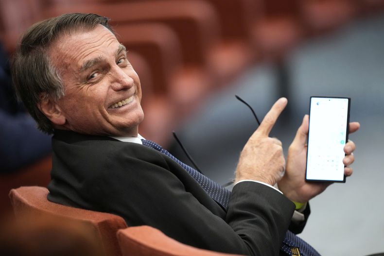El expresidente de Brasil Jair Bolsonaro muestra la pantalla de su teléfono durante su juicio ante el Supremo Tribunal Federal mientras él y otras personas enfrentan cargos por un supuesto complot golpista para mantenerlo en el poder después de su derrota electoral de 2022, el martes 10 de junio de 2025, en Brasilia. (AP Foto/Eraldo Peres)