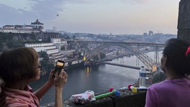 Gente apoya sus martillos de plástico en un muro mientras mira faroles flotantes sobre el río Duero, mientras la ciudad norteña de Oporto, en Portugal, se prepara para celebrar la víspera de San Juan, la tarde del lunes 23 de junio de 2025. (AP Foto/Helena Alves)