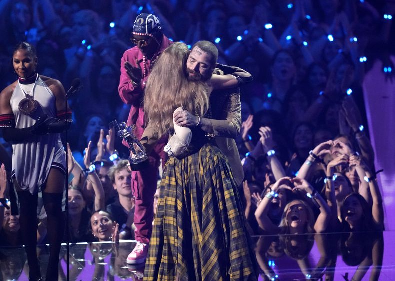 Taylor Swift, centro, y Post Malone se abrazan al aceptar el premio a la mejor colaboración por Fortnight durante los MTV Video Music Awards el miércoles 11 de septiembre de 2024 en el UBS Arena de Elmont, Nueva York. Jordan Chiles, extremo izquierdo, y Flava Flav mira. (Foto Charles Sykes/Invision/AP)