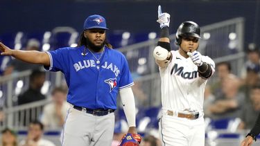 Luis Arráez, derecha, de los Marlins de Miami, reacciona después de batear un sencillo durante la primera entrada del juego de béisbol en contra de los Azulejos de Toronto, el lunes 19 de junio de 2023, en Miami. El primera base de Azulejos, Vladimir Guerrero Jr., izquierda, observa. (AP Foto/Lynne Sladky)