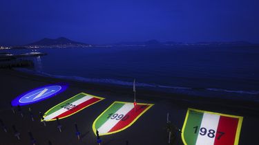 El escudo del Napoli y tres Scudettos referentes a sus dos títulos anteriores y al que podría conseguir, se proyectan en la playa de Posillipo, el jueves 27 de abril de 2023 (Alessandro Garofalo/LaPresse via AP)