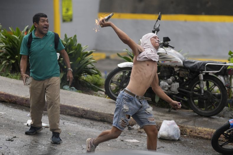 Ciudadanos lanzan objetos a la agentes de la Guardia Nacional en protesta por los resultados oficiales el día después de las elecciones presidenciales en Caracas, Venezuela, el lunes 29 de julio de 2024. (AP Foto/Cristian Hernández)