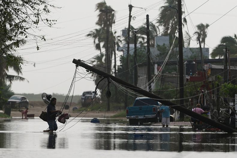 Un hombre transporta objetos a través de aguas inundadas, pasando junto a líneas eléctricas derribadas tras el paso del huracán Polo en Puerto San Carlos, estado de Baja California Sur, México, el martes 29 de septiembre de 2026. (Foto AP/Eduardo Verdugo)