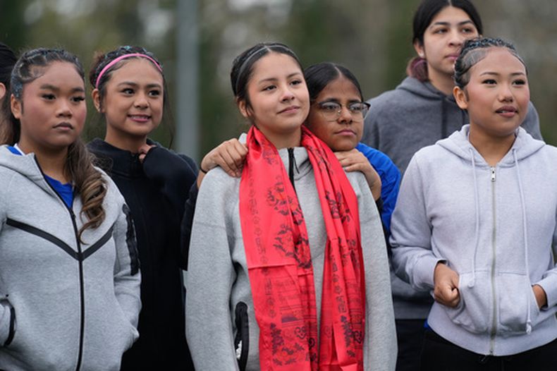 Samira Abdul apoya su cabeza en el hombro de Valeria Hernandez, centro, mientras ambas están con sus compañeras previo a un partido de fútbol del torneo para niñas inmigrantes y refugiadas el dominco 29 de marzo de 2026, en Portland, Oregon. A Valeria, su madre y su hermana menor les regalaron bufandas coloridas como muestra de apoyo. (AP Foto/Jenny Kane)