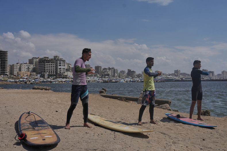 Los palestinos Tahseen Abu Assi (izquierda), Khalil Abu Jayyab (centro) y Abed Rahim Alostaz calientan antes de surfear en la playa en la Ciudad de Gaza, el 4 de mayo de 2026. (AP Foto/Jehad Alshrafi)