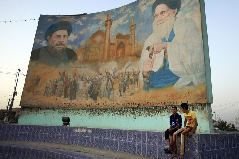 ARCHIVO – Dos niños sentados frente a un mural de los clérigos chiíes Mohammad Baqir al-Sadr, izquierda, y Mohammad Sadiq al-Sadr, derecha, en Bagdad, Irak, pintado sobre un retrato del exdictador Saddam Hussein, el sábado 6 de abril de 2013. (AP Foto/Karim Kadim, Archivo)