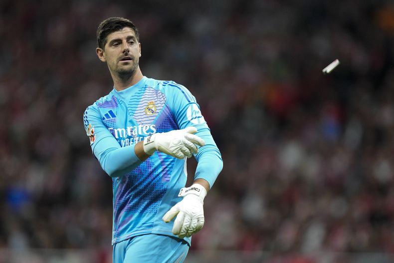 El arquero del Real Madrid Thibaut Courtois saca de la cancha un encendedor arrojado por hinchas del Atlético de Madrid durante el partido contra Real Madrid, el domingo 29 de septiembre de 2024. (AP Foto/Bernat Armangue)
