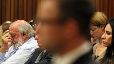 americateve | Barry Steenkamp (izquierda), padre de Reeva Steenkamp, se toca la cara mientras Oscar Pistorius (borroso en primer plano), asiste a una sesi&oacute;n de la vista para la sentencia del caso, en Pretoria, Sud&aacute;frica, el 14 de octubre de 2014. (Foto AP