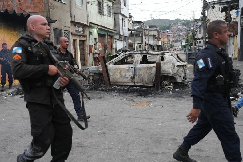 Policías pasan junto a un coche quemado que fue utilizado como barricada durante una operación policial contra presuntos narcotraficantes en la favela Complexo do Alemao, donde opera la organización criminal Comando Vermelho, en Río de Janeiro, el martes 28 de octubre de 2025. (AP Foto/Silvia Izquierdo)