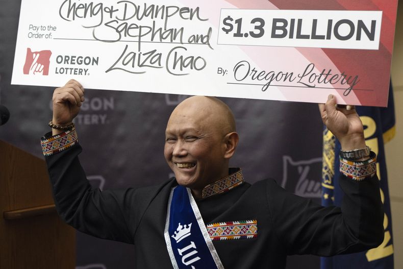 Cheng Saephan levanta un cheque después de hablar en una conferencia de prensa el lunes 29 de abril de 2024 en las oficinas de la Lotería de Oregon, en Salem, Oregon, en la que se reveló que fue uno de los ganadores del premio de 1.300 millones de dólares de la lotería Powerball. (AP Foto/Jenny Kane)