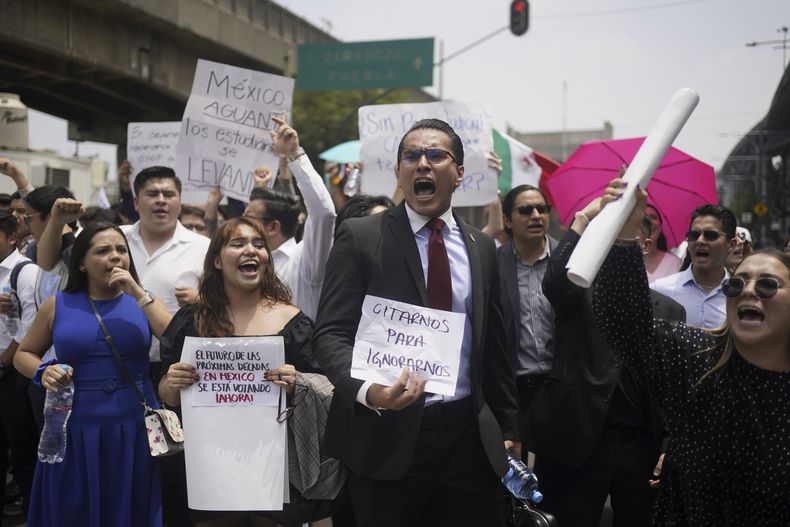 Estudiantes de Derecho bloquean una calle para protestar contra una propuesta de reforma legal que haría que los jueces tuviesen que ser elegidos, en el exterior del centro deportivo donde se reúnen los legisladores debido a las manifestaciones que bloquean el acceso al edificio del Congreso, en la Ciudad de México, el 3 de septiembre de 2024. Los carteles dicen Citarnos para ignorarnos y El futuro de las próximas décadas en México se está votando ahora. (AP Foto/Félix Márquez)