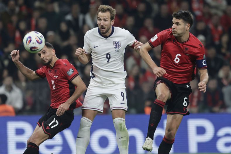 Harry Kane, de Inglaterra, al centro, anota el segundo gol de su equipo mientras Naser Aliji, a la izquierda, y Berat Djimsiti, de Albania, intentan detenerlo durante el juego de fútbol del grupo K de clasificación para la Copa del Mundo de 2026 entre Albania y Inglaterra, en Tirana, Albania, el domingo 16 de noviembre de 2025. (AP Photo/Vlasov Sulaj)