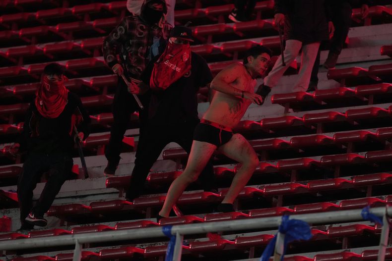 Fanáticos del Independiente, de Argentina, atacan a un seguidor del Universidad de Chile justo después de despojarlo de su ropa en el partido de vuelta de los octavos de final de la Copa Sudamericana en el estadio Libertadores de América, en Avellaneda, Argentina, el 20 de agosto de 2025. (AP Foto/Gustavo Garello)