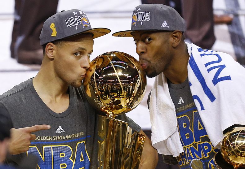 ARCHIVO- Stephen Curry, izquierda, y Andre Iguodala, de los Warriors de Golden State besan el trofeo Larry OBrien después de derrotar a los Cavaliers de Cleveland 105-97 en el Juego 6 de las Finales de la NBA en Cleveland, el 17 de junio de 2015. Iguodala, cuatro veces campeón de la NBA con los Warriors de Golden State durante 19 años de carrera, se retira.(AP Foto/Paul Sancya, Archivo)