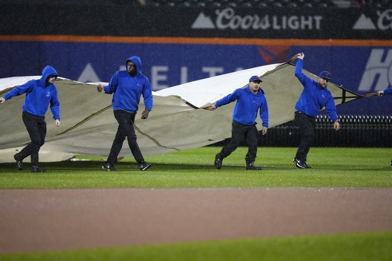 Empleados cubren el terreno de juego durante una suspensión por lluvia en el duelo entre los Mets de Nueva York y los Marlins de Miami, el viernes 29 de septiembre de 2023, en Nueva York. (AP Foto/Frank Franklin II)