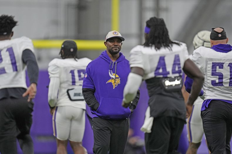 ARCHIVO - Brian Flores, centro, coordinador defensivo de los Vikings de Minnesota, está parado en el campo durante un entrenamiento del equipo de la NFL en Eagan, Minnesota, el miércoles 30 de octubre de 2024. (AP Foto/Abbie Parr, Archivo)