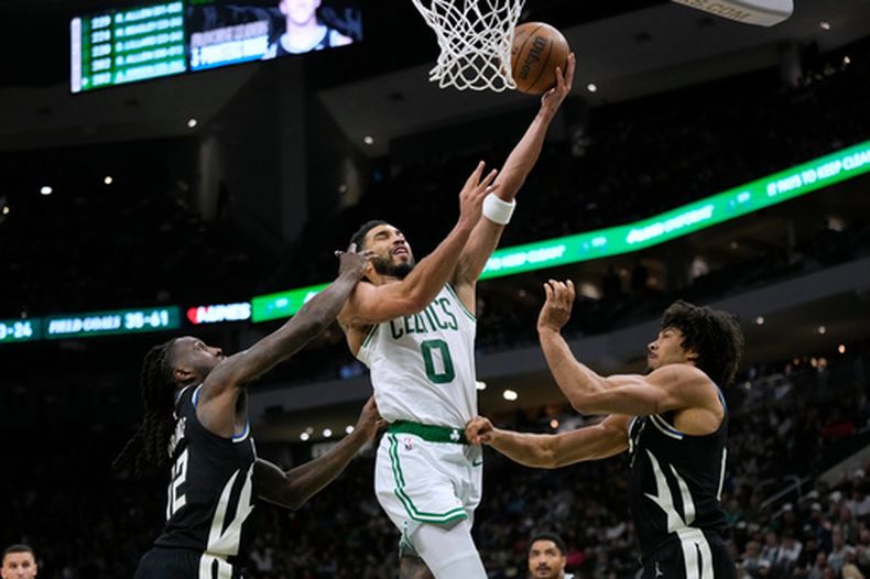 Jayson Tatum (0), de los Celtics de Boston, se cuela para encestar entre Taurean Prince y Jericho Sims, de los Bucks de Milwaukee, durante la segunda mitad del juego de balocnesto de la NBA, el viernes 3 de abril de 2026, en Milwaukee. (AP Foto/Aaron Gash)