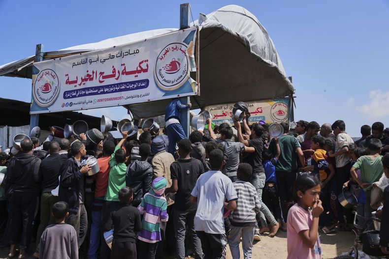 Niños y adultos palestinos tratan de conseguir comida en una cocina comunitaria en Jan Yunis, en la Franja de Gaza, el lunes 5 de mayo de 2025. (AP Foto/Abdel Kareem Hana)
