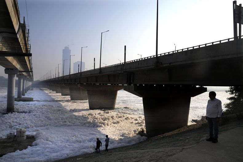 Gente de pie entre el smog de la mañana junto a un puente sobre el río Yamuna cubierto de contaminación, al día siguiente del festival hindú de Diwali, en Nueva Delhi, India, el viernes 1 de noviembre de 2024. (AP Foto/Manish Swarup)