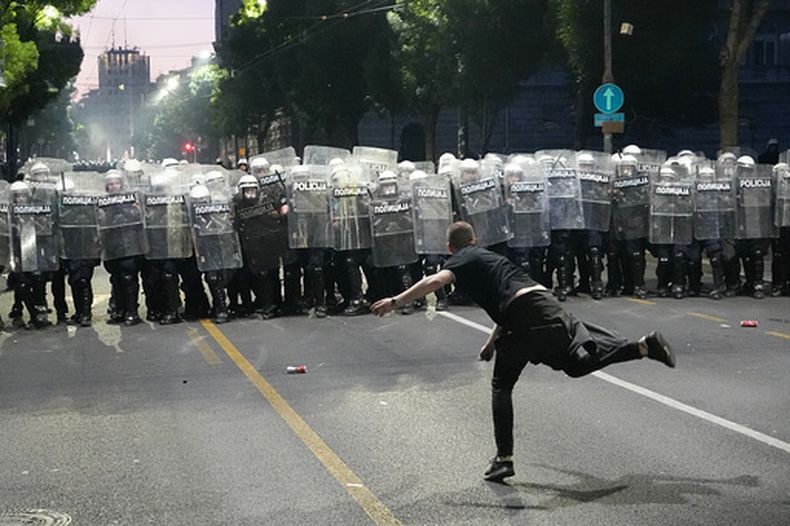 Un hombre arroja una piedra contra la policía antidisturbios mientras estallan los choques durante una manifestación encabezada por estudiantes universitarios serbios que exigen importantes cambios políticos en el país balcánico, gobernado por el presidente President Aleksandar Vucic, en Belgrado, Serbia, el sábado 23 de mayo de 2026. (AP Foto/Darko Vojinovic)