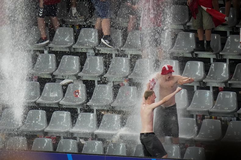 Un par de aficionados bailan bajo la lluvia, durante una interrupción del partido entre Alemania y Dinamarca en la Euro, el sábado 29 de junio de 2024. (AP Photo/Hassan Ammar)