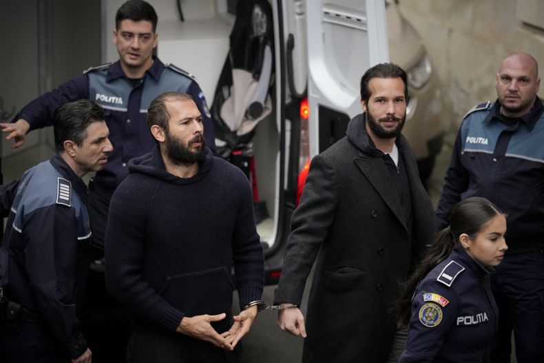 ARCHIVO - La policía escolta a Andrew Tate, en el centro, esposado a su hermano, Tristan Tate, hacia la Corte de Apelaciones de Bucarest, Rumanía, el lunes 27 de febrero de 2023. (AP Foto/Andreea Alexandru, Archivo)