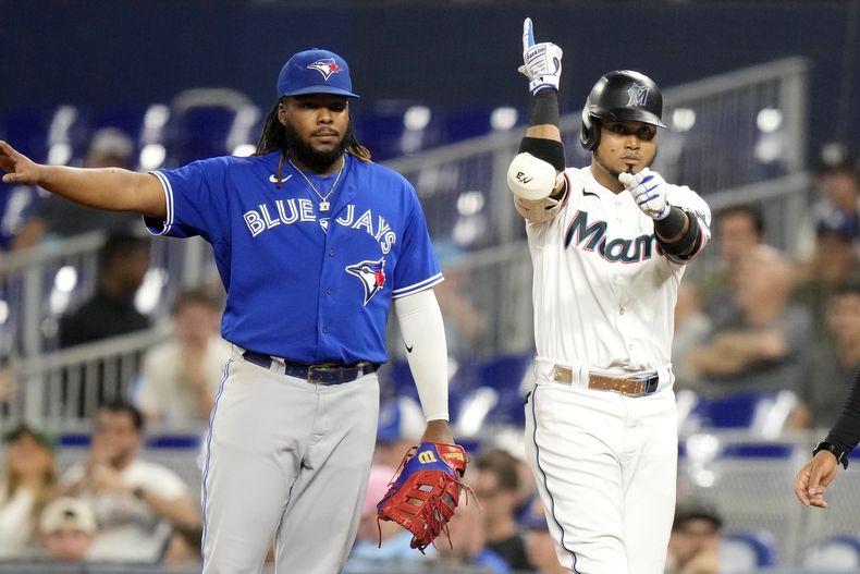 Luis Arráez, derecha, de los Marlins de Miami, reacciona después de batear un sencillo durante la primera entrada del juego de béisbol en contra de los Azulejos de Toronto, el lunes 19 de junio de 2023, en Miami. El primera base de Azulejos, Vladimir Guerrero Jr., izquierda, observa. (AP Foto/Lynne Sladky)