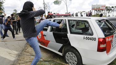 americateve | Un manifestante enmascarado golpea un veh&iacute;culo policial vac&iacute;o cerca del laboratorio Instituto Royal en protesta por la prueba de drogas con animales en Sao Roque, Brasil, el s&aacute;bado, 19 de octubre del 2013. (Foto AP/Nelson Antoine)