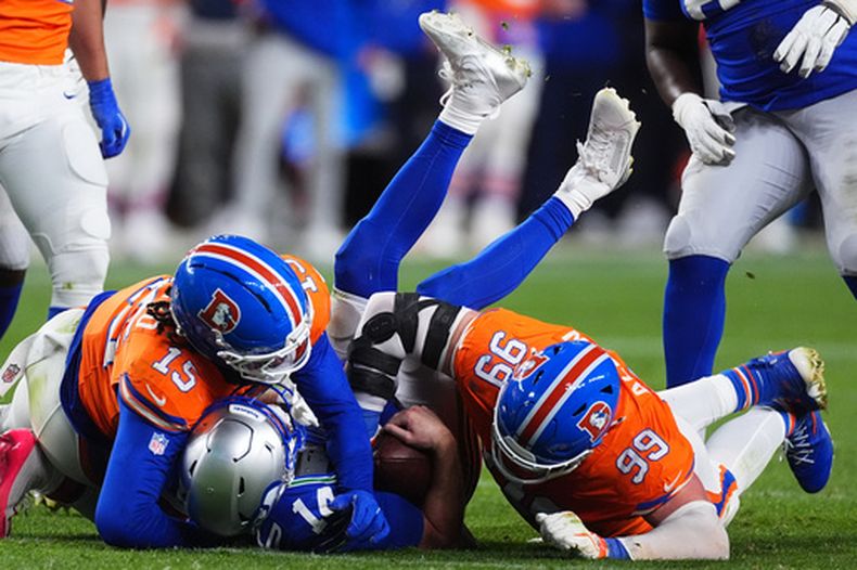 Zach Allen (99) y Nik Bonitto (15), de los Broncos de Denver, aplastan a Sam Darnold, quarterback de los Seahawks de Seattle, durante la segunda mitad del partido de la NFL, el jueves 15 de octubre de 2026, en Denver. (AP Foto/David Zalubowski)