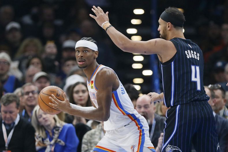 Shai Gilgeous Alexander (izquierda), base del Thunder de Oklahoma City, busca enviar un pase junto a Jalen Suggs, del Magic de Orlando, el sábado 13 de enero de 2024 (AP Foto/Nate Billings)