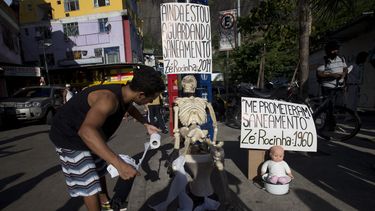 americateve | Un hombre obsequia papel sanitario a un esqueleto durante una manifestaci&oacute;n en la favela de Rocinha, a favor del tratamiento de aguas de alba&ntilde;al en ese barrio pobre ubicado en R&iacute;o de Janeiro, Brasil, el s&aacute;bado 22 de febrero de
