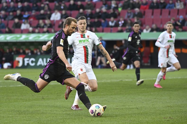 Harry Kane del Bayern Munich dispara el balón superando a Jeffrey Gouweleeuw del Augsburg en el encuentro de la Bundesliga el sábado 27 de enero del 2024. (Sven Hoppe/dpa via AP)