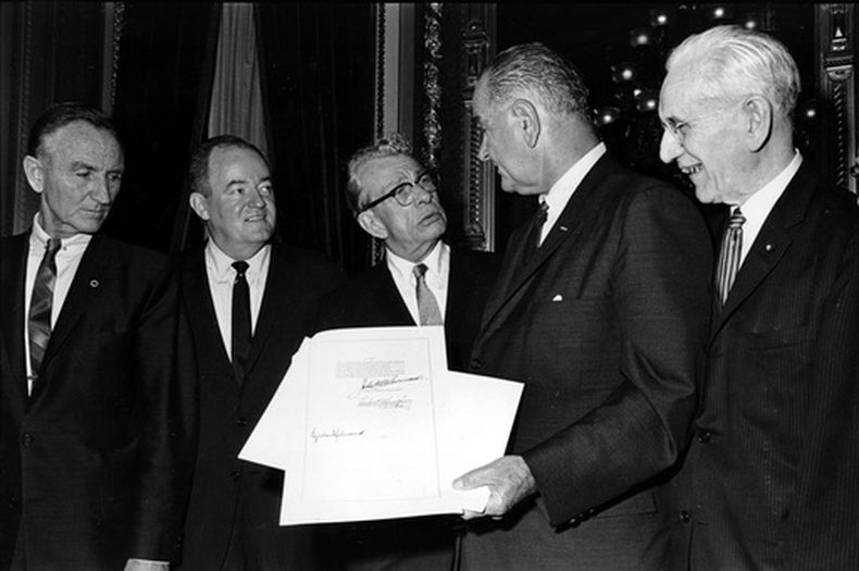 ARCHIVO - El presidente de Estados Unidos Lyndon B. Johnson, sostiene el documento firmado que sanciona la Ley de Derecho al Voto de 1965, mientras habla con el senador republicano de Illinois Everett Dirksen, en la Sala Presidencial, en Washington, el 6 de agosto de 1965. Las firmas que aparecen en el documento son las de Johnson (abajo, izquierda); el presidente de la Cámara de Representantes, John McCormack (arriba, derecha), y la del vicepresidente, Hubert Humphrey (abajo, segunda por la izquierda). En la esquina de la izquierda de la imagen aparece el senador Mike Mansfield. (AP Foto)