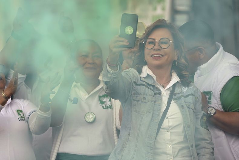 La candidata presidencial Sandra Torres, del partido UNE, sostiene un teléfono celular en medio de humo verde al cerrar su campaña en el mercado La Terminal en Ciudad de Guatemala, el viernes 18 de agosto de 2023. (AP Foto/Moisés Castillo)