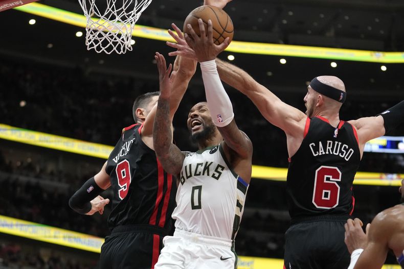 Damian Lillard de los Bucks de Milwaukee avanza hacia la canasta bajo presión de Nikola Vucevic y Alex Caruso de los Bulls de Chicago en el el encuentro del 30 de noviembre del 2023. (AP Foto/Charles Rex Arbogast)
