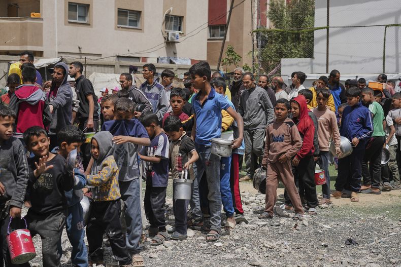 Varios palestinos esperan en fila para recibir comida donada en un centro de distribución en Nuseirat, en el centro de la Franja de Gaza, el viernes 11 de abril de 2025. (AP Foto/Abdel Kareem Hana)