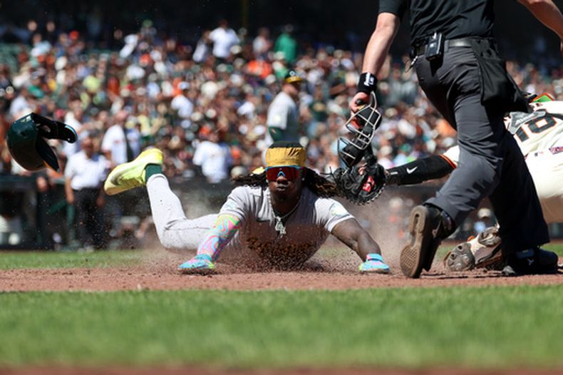 Lawrence Butler (centro), de los Atléticos, se desliza a salvo en el plato ante el receptor de los Gigantes de San Francisco, Eric Haase (18), tras un sencillo conectado por Jeff McNeil durante la octava entrada de un partido de béisbol en San Francisco, el jueves 25 de junio de 2026. (Foto AP/Jed Jacobsohn)