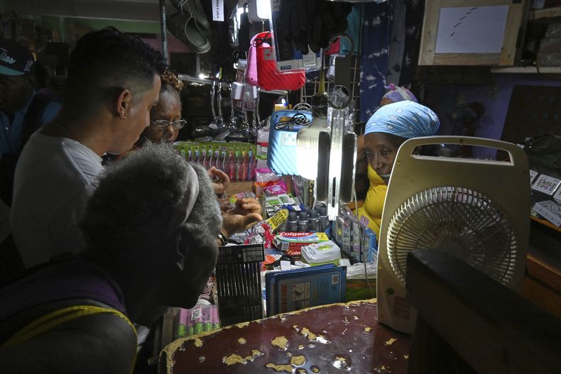 Un comerciante utiliza lámparas recargables para iluminar mientras atiende a clientes durante un apagón, dentro de una ferretería privada, en La Habana, Cuba, el martes 15 de julio de 2025. (Foto AP/Jorge Luis Baños)