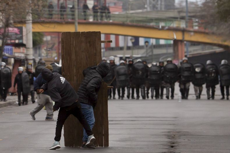 Manifestantes se refugian tras un tablero de madera durante enfrentamientos con la policía en San Salvador de Jujuy, Argentina, el martes 20 de junio de 2023. Las movilizaciones detonaron en la provincia de Jujuy en reacción a una reforma de la constitución provincial reciente criticada por sus restricciones a la protesta social. (AP Foto/Javier Corbalán)