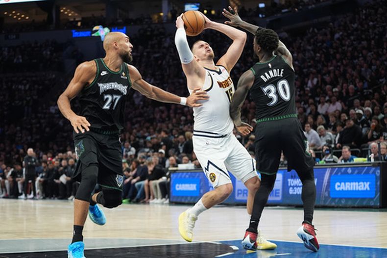 El pívot de los Nuggets de Denver, Nikola Jokic (15), avanza hacia la canasta mientras el pívot de los Timberwolves de Minnesota, Rudy Gobert (27), y el alero Julius Randle (30) defienden durante la primera mitad del tercer juego de una serie de la primera ronda de los playoffs de la NBA, el jueves 23 de abril de 2026, en Mineápolis. (AP Foto/Abbie Parr)