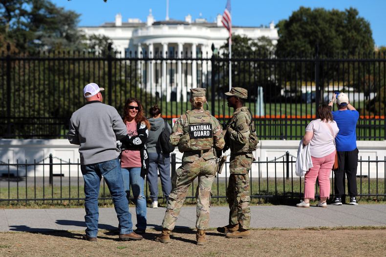 ARCHIVO – Varias personas hablan con efectivos de la Guardia Nacional en The Ellipse, con la Casa Blanca en el fondo, el 17 de octubre de 2025, en Washington. (AP Foto/Rahmat Gul, Archivo)