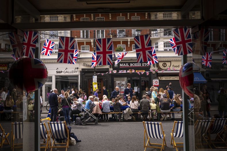 Varias personas comen su almuerzo en grandes mesas colocadas en la calle como parte de las celebraciones por la coronación del rey Carlos III, el domingo 7 de mayo de 2023, en Londres. (AP Foto/Emilio Morenatti)