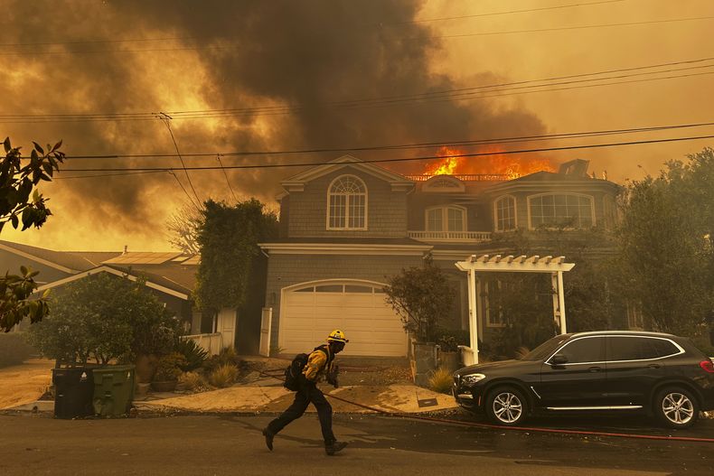 Una residencia en llamas mientras un bombero combate un incendio en Pacific Palisades, el martes 7 de enero de 2025, en Los Ángeles. (AP Foto/Eugene Garcia)
