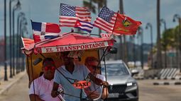 Pasajeros viajan en un bicitaxi adornado con las banderas de Estados Unidos, Cuba y la República Dominicana, el miércoles 20 de mayo de 2026, en La Habana, Cuba. (AP Foto/Ramón Espinosa)