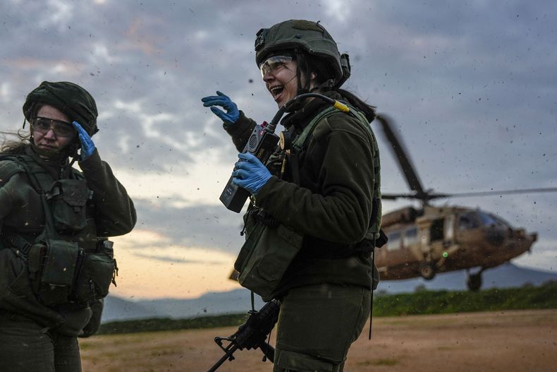 Paramédicas militares israelíes se resguardan del viento provocado por el aterrizaje de un helicóptero militar durante un simulacro de evacuación de personas heridas, el martes 20 de febrero de 2024, en el norte de Israel, cerca de la frontera con Líbano. (AP Foto/Ariel Schalit)