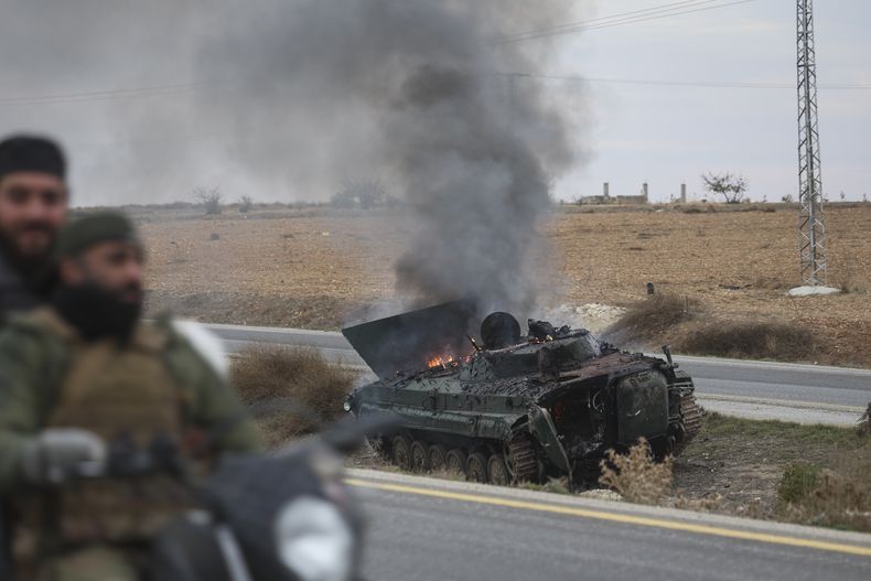 Rebeldes sirios pasan junto a un vehículo blindado incendiado al sur de Hama, Siria, el sábado 7 de diciembre de 2024. (AP Foto/Ghaith Alsayed)