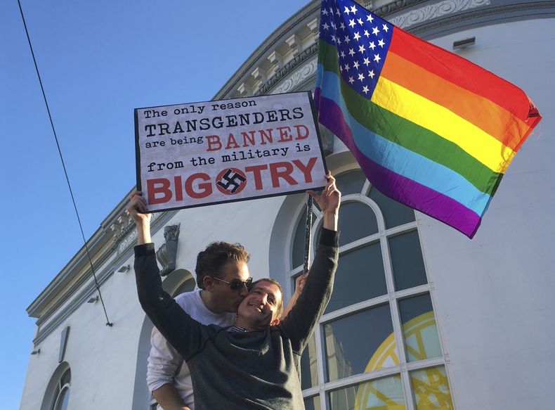 ARCHIVO - Nick Rondoletto, izquierda, y Doug Thorogood, ambos de San Francisco, ondean una bandera multicolor y sostienen un cartel durante una protesta realizada en San Francisco el miércoles 26 de julio de 2017 para oponerse a una propuesta para prohibir que personas transgénero presten servicio en el ejército de EEUU. (AP Foto/Olga R. Rodriguez, Archivo)