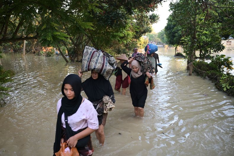La gente lleva sus pertenencias mientras cruza el agua en una aldea inundada en Bireun, provincia de Aceh, Indonesia, sábado 29 de noviembre de 2025. (Foto AP/Reza Saifullah)